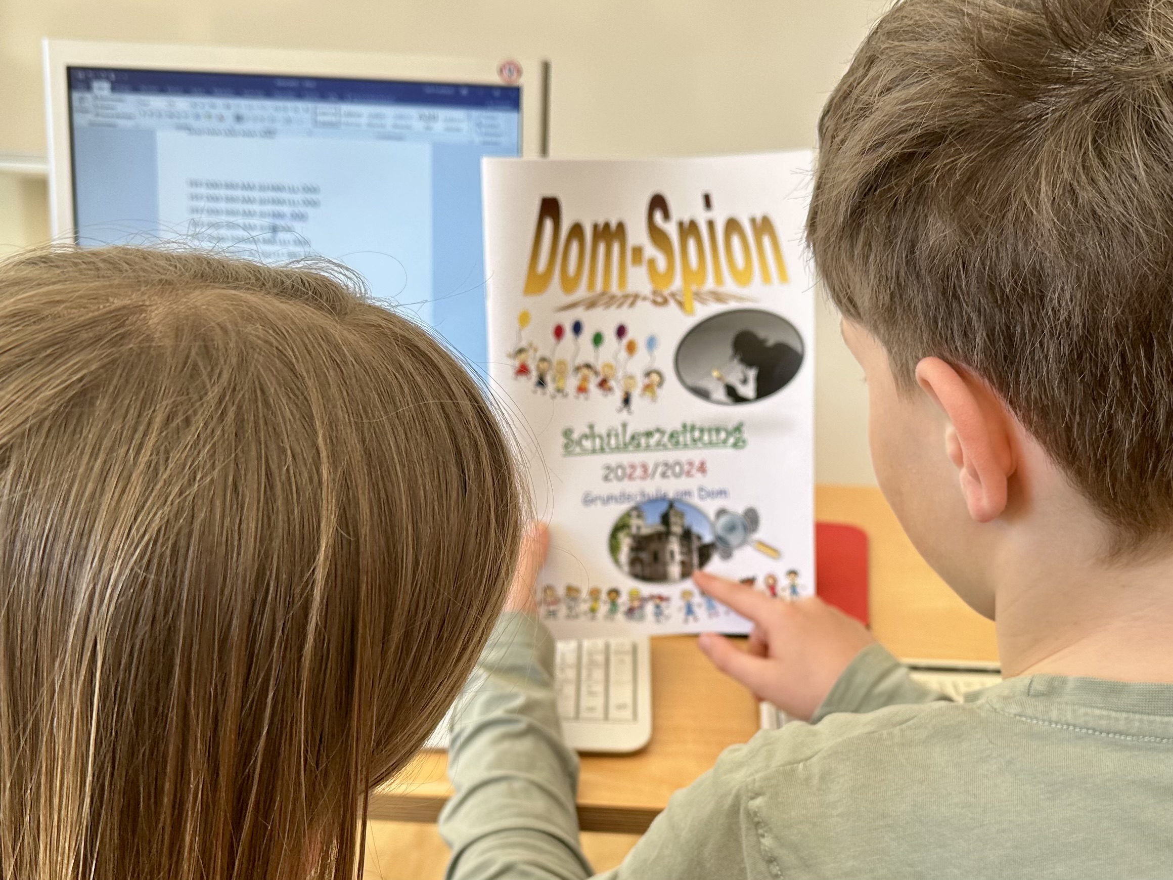 Zwei Kinder betrachten das Deckblatt der Schülerzeitung der Grundschule am Dom: Dom-Spion