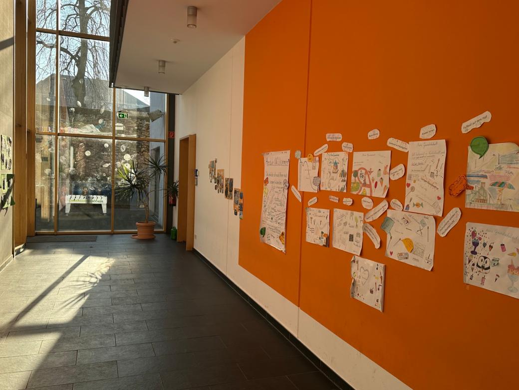 Man schaut in den Flur im Erdgeschoss der Grundschule am Dom. An der rechten Flurseite sind Erinnerungsplakate zu sehen. Am Flurende ist eine Glaswand zum Schulhof.