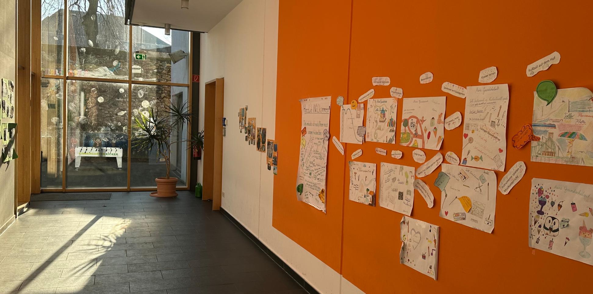 Man schaut in den Flur im Erdgeschoss der Grundschule am Dom. An der rechten Flurseite sind Erinnerungsplakate zu sehen. Am Flurende ist eine Glaswand zum Schulhof.
