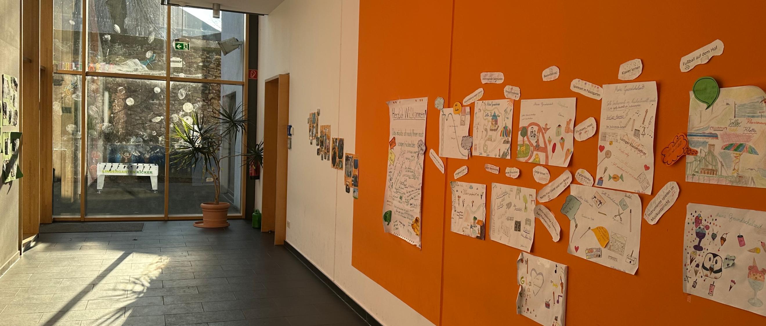 Man schaut in den Flur im Erdgeschoss der Grundschule am Dom. An der rechten Flurseite sind Erinnerungsplakate zu sehen. Am Flurende ist eine Glaswand zum Schulhof.