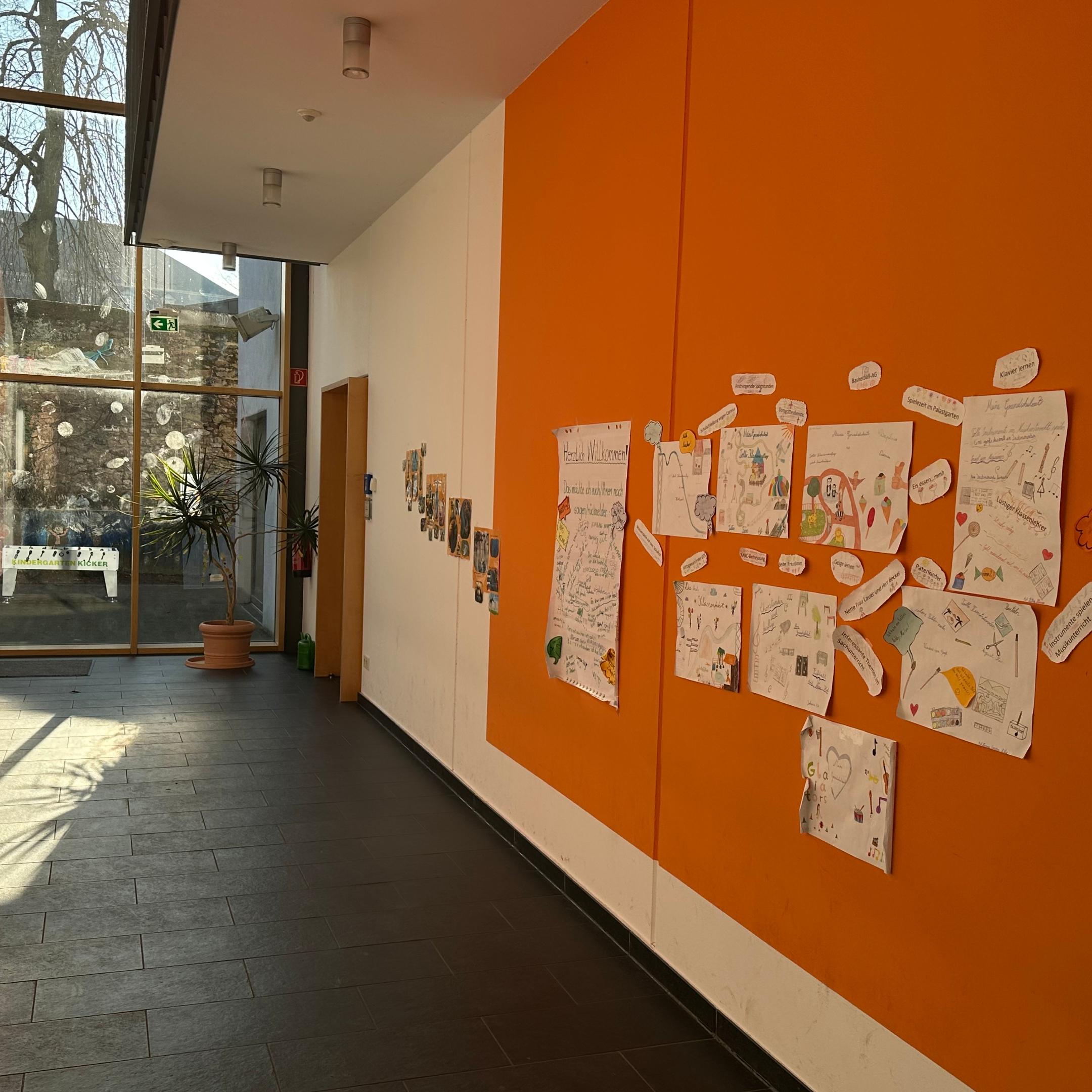 Man schaut in den Flur im Erdgeschoss der Grundschule am Dom. An der rechten Flurseite sind Erinnerungsplakate zu sehen. Am Flurende ist eine Glaswand zum Schulhof.