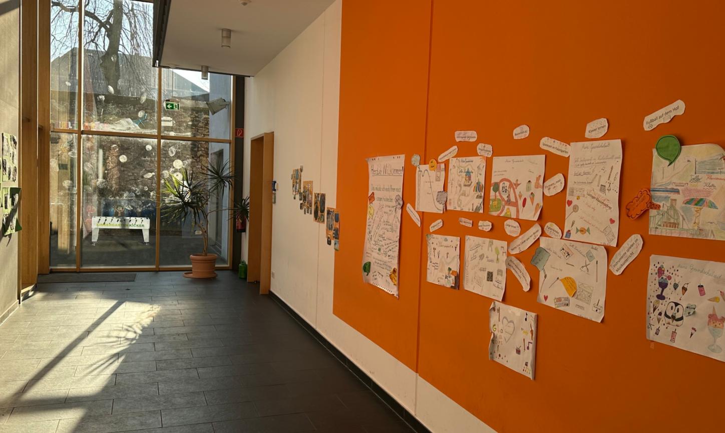 Man schaut in den Flur im Erdgeschoss der Grundschule am Dom. An der rechten Flurseite sind Erinnerungsplakate zu sehen. Am Flurende ist eine Glaswand zum Schulhof.