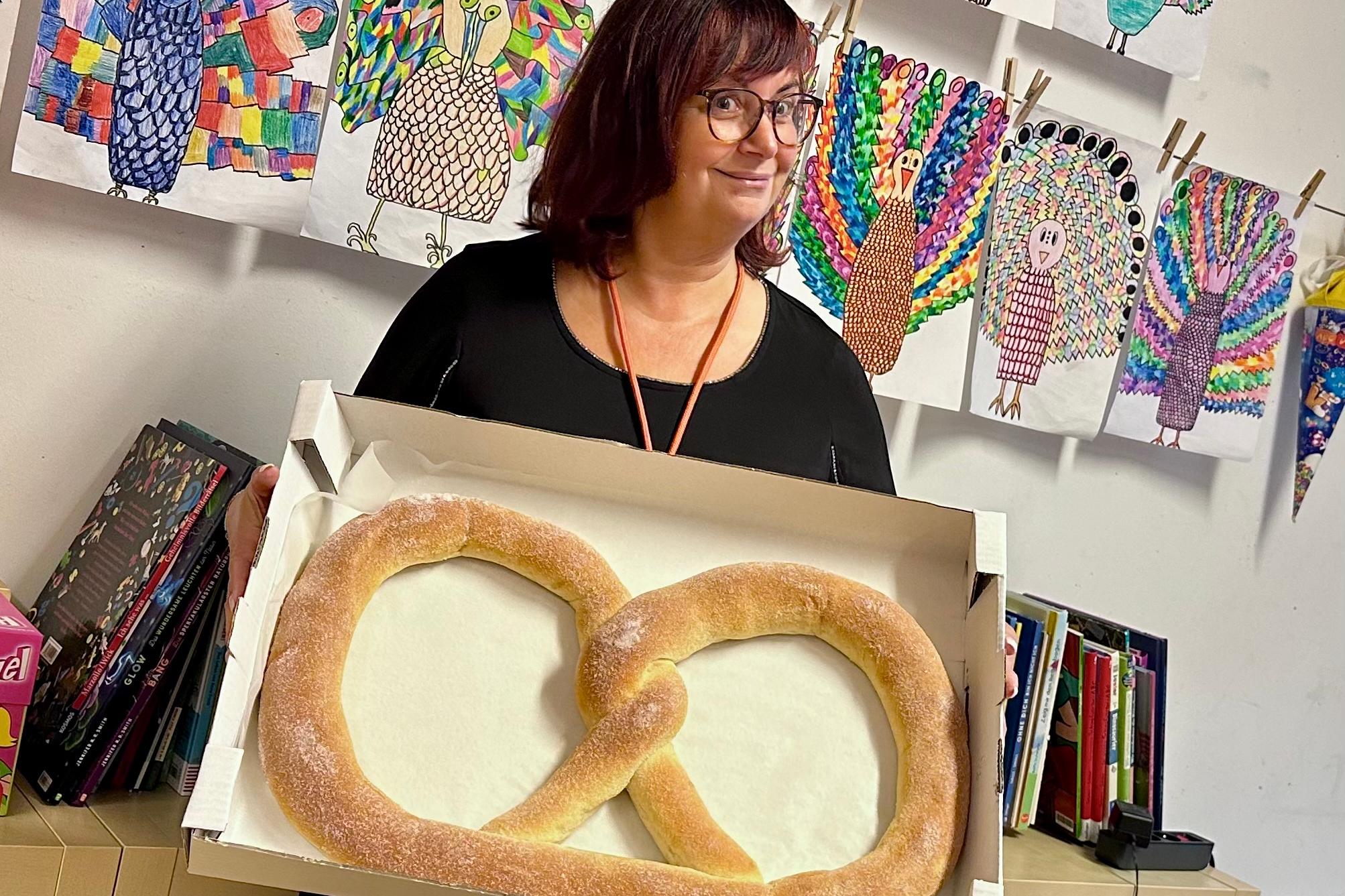 Lehrerin Heiderich hält eine riesige Martinsbrezel für ihre Klasse in die Kamera