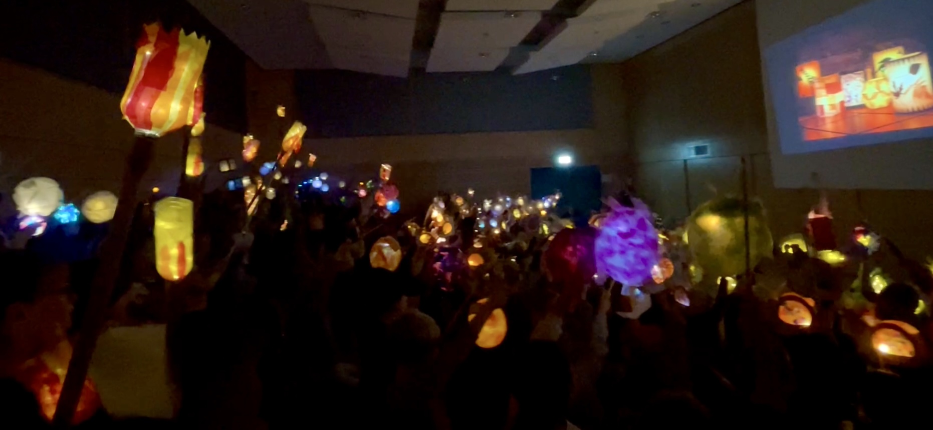 Blick auf leuchtende Laternen, die in der Aula der GS am Dom von Kindern in die Höhe gehalten werden