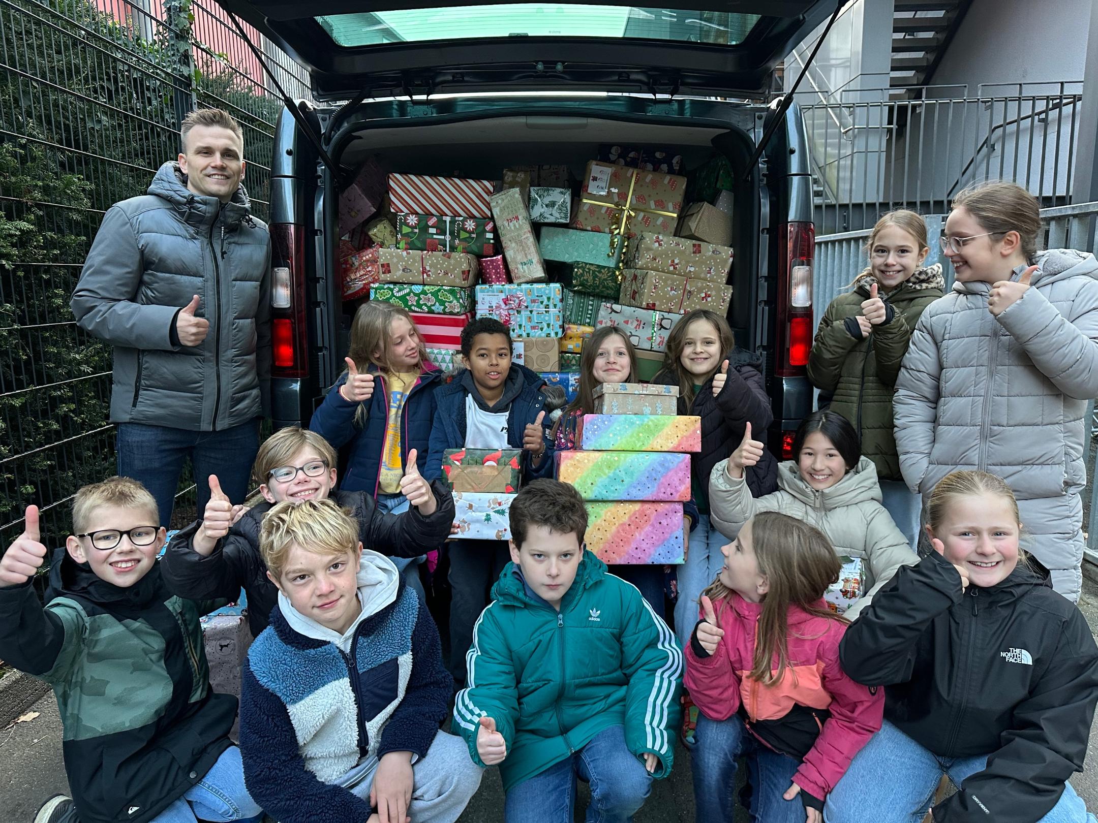 Herr Dauns (Round Table Deutschland) und Kinder der GS am Dom vor einem mit vielen Päckchen gefüllten Transporter