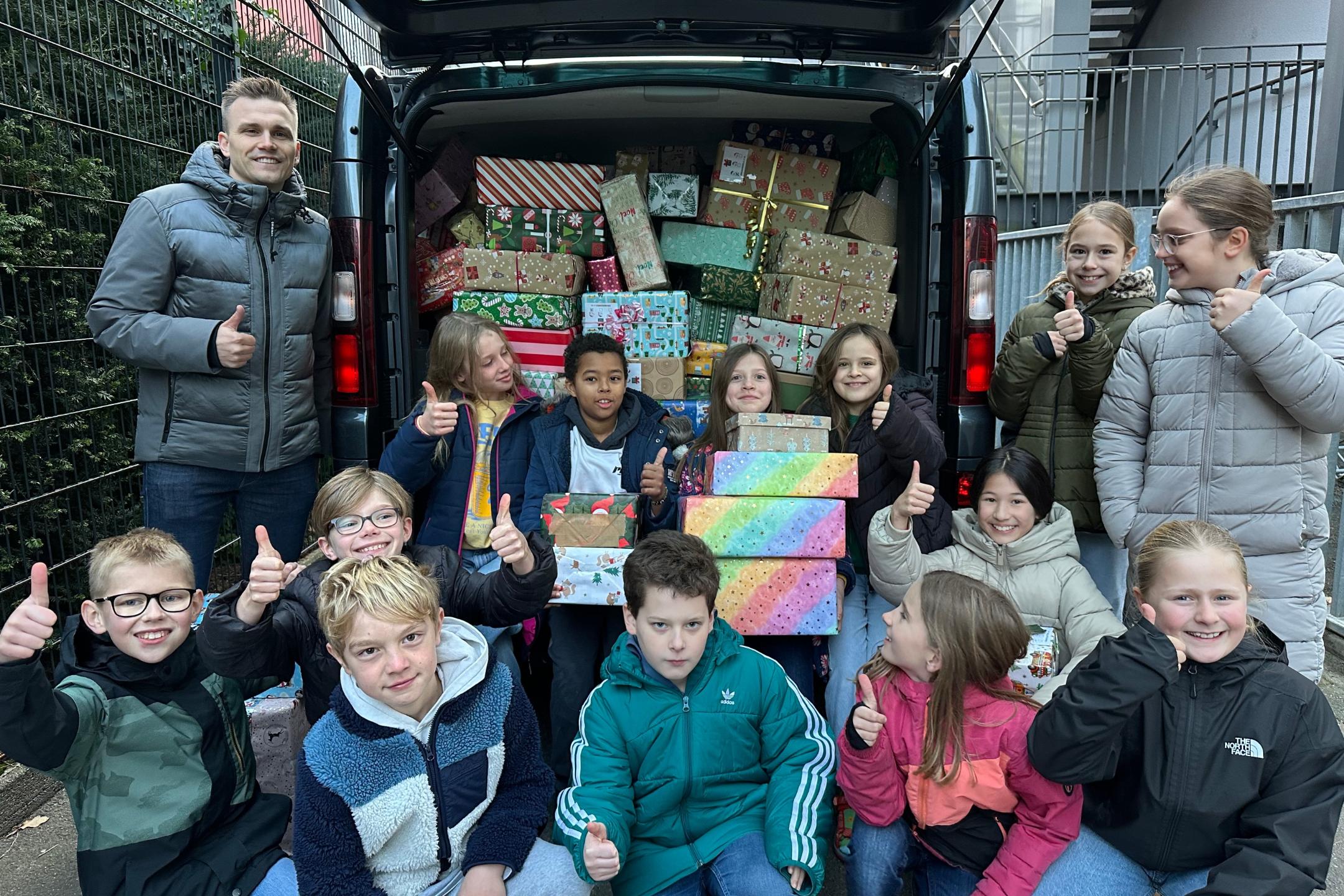 Herr Dauns (Round Table Deutschland) und Kinder der GS am Dom vor einem mit vielen Päckchen gefüllten Transporter