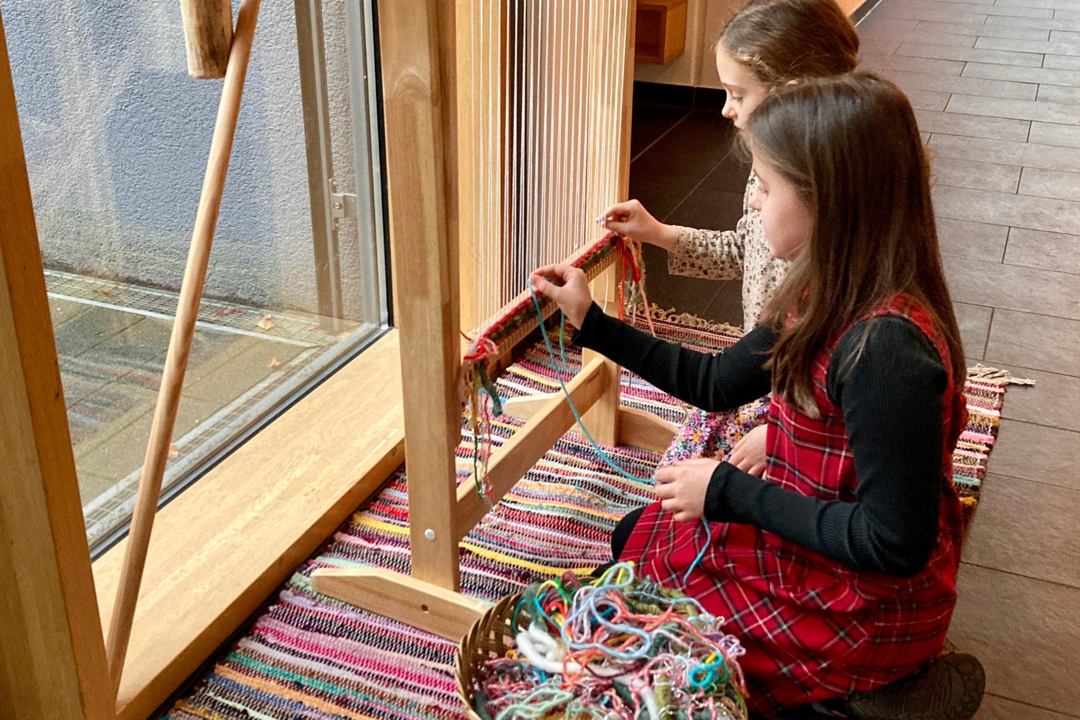 Kinder weben an einem riesigen Webrahmen aus einzelnen Fäden einen Teppich